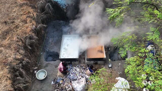 Natore, Bangladesh - 13 March 2024: Aerial view of workers boiling date palm juice in large vats to produce traditional jaggery with thick smoke rising in Natore.