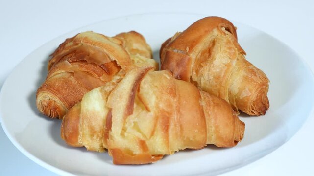 Croissant-shaped breads on a white background, shot from a rotating platform in slow motion. Close up