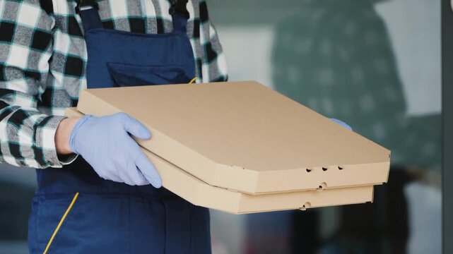 Delivery person wearing gloves holds stacked pizza boxes, preparing for contactless delivery.
