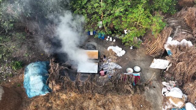 Natore, Bangladesh - 13 March 2024: Aerial view of workers boiling date juice in large pans to produce molasses in a rural village surrounded by lush trees and straw.