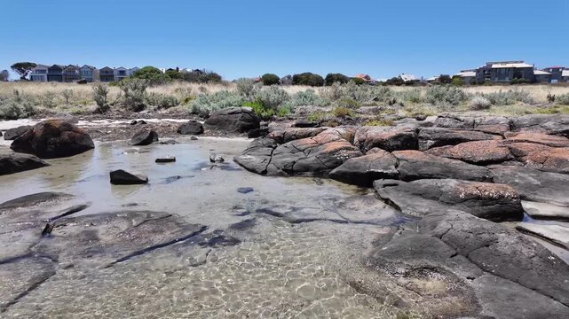 Rock pools, clear shallow sea water and a distant line of residential coastal properties atJawbone Marine Sanctuary in Williamstown, Melbourne Australia.