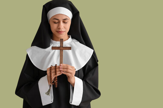 Young nun praying with wooden cross and rosary beads, eyes closed in peaceful devotion, female religious portrait in black and white habit isolated on plain background