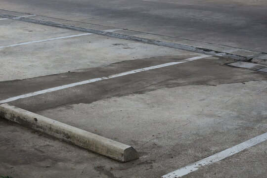 Empty concrete parking lot with white lines and a wheel stop