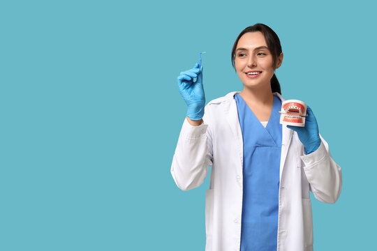 Young female dentist with brush for cleaning braces and jaw model on blue background
