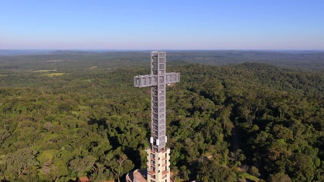 Monumental cross tower rises above Atlantic Forest canopy in Parque Tem&aacute;tico de la Cruz, Santa Ana, Misiones Province, Northeast Argentina, drone push in aerial shot during sunny daylight conditions.