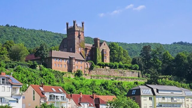 Historic hilltop castle in Neckarsteinach, Germany, overlooking village rooftops and green forested hills under a clear blue sky, scenic view of medieval architecture in the Neckar Valley.
