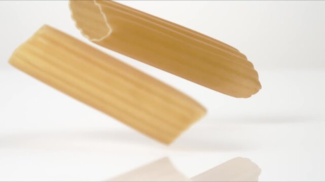 Fresh uncooked Manicotti bouncing on a white tabletop in slow motion close up macro before settling.