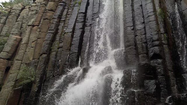 Waterfall flowing down tall basalt rock formations surrounded by natural landscape and rugged volcanic cliff texture in scenic environment
