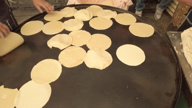 Close view of workers preparing fresh tortillas by hand on large heated griddle inside busy traditional Mexican food cooking area