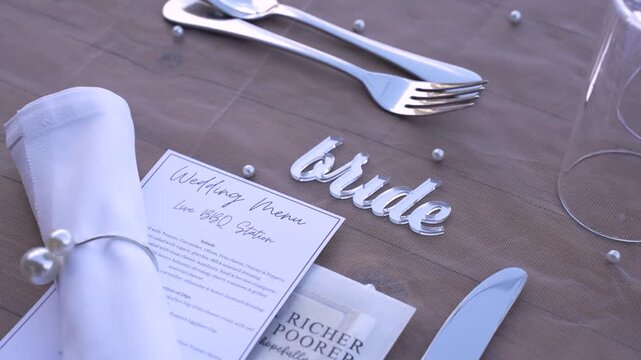 A table is prepared for a wedding event. The setup includes a menu, silverware, and decorative items. It shows a cozy dining area designed for guests to enjoy their meal together.