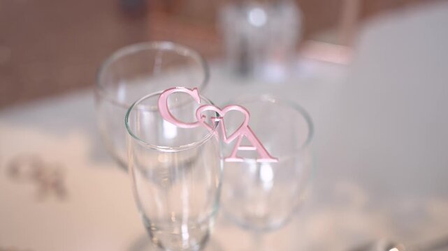 Two glasses are placed on a table, with a decorative piece showing initials that belong to a couple. The setting looks festive and is likely part of a celebration event.