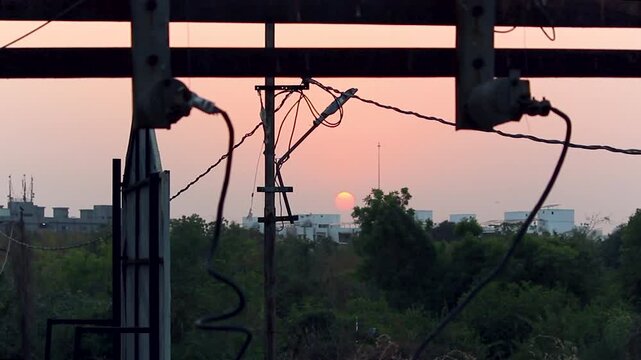 Atmospheric sunset view through electrical wires and urban structures, ideal for city life, infrastructure, energy themes, industrial storytelling, and cinematic evening visuals.