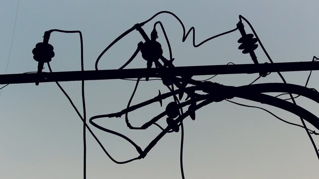 Close-up silhouette of tangled electrical wires and utility infrastructure against the sky, ideal for energy, urban infrastructure, electricity distribution, and industrial documentary projects.