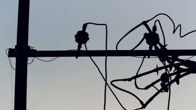 Close up silhouette of tangled electrical wires and utility pole infrastructure against clear sky, ideal for energy, electricity, urban infrastructure, power supply, and industrial themes.