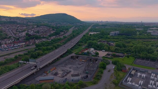 Port Talbot in Early Morning with Cars on Motorway and nearby Substation with BESS Battery Storage Containers. Energy for nearby Houses Using Sustainable Power Solutions. Wales, UK.
