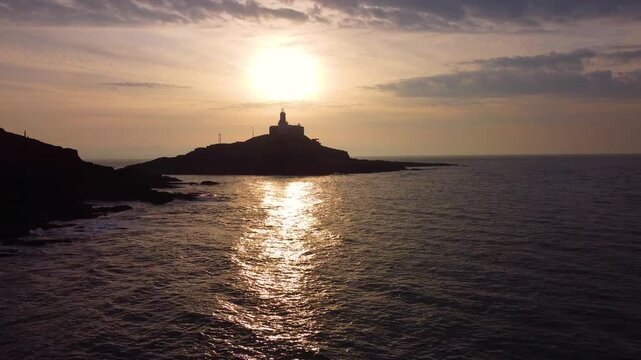 Static Aerial of Mumbles Lighthouse at Sunrise. Golden Reflection of Sun on Ocean with Dynamic Clouds. Perfect for tourism, travel documentaries. Wales, UK. 4K.