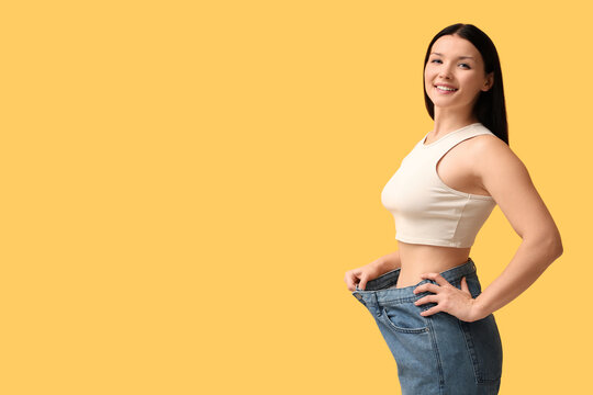Beautiful young happy woman in loose jeans on yellow background. Weight loss concept