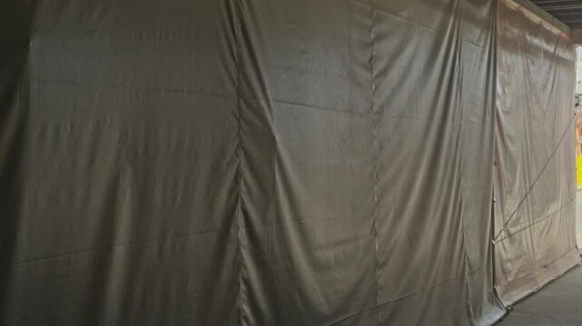 A close-up shot of a large, heavy-duty brown tarpaulin stretched tightly to cover an outdoor structure. The texture of the fabric and the tension in the material are clearly visible.