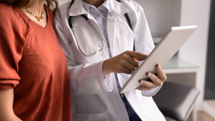 Close up shot of medical specialist using tablet consulting female patient, accessing digital...