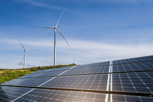 Solar panels and wind turbines generator in renewable energy farm with blue sky background for sustainable development.
