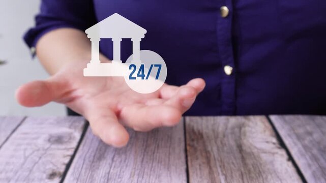 Close-up of a woman's hand on a table holding an animated bank icon with a button that says 24/7. Cash availability 24 hours a day, 7 days a week.