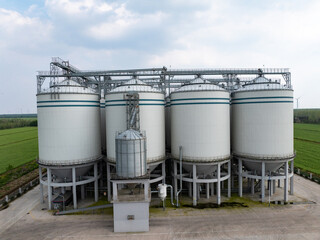 Obraz premium Large white industrial silos for grain storage standing in a green field under cloudy sky