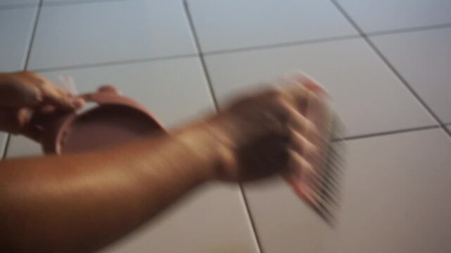 Close-up video of a person sweeping white ceramic tile floor indoors using a hand broom. Daily household cleaning activity in a minimalist home with natural lighting, showing hygiene, cleanliness, and