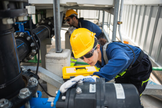 Professional technician and worker performing maintenance on industrial HVAC and piping system on commercial rooftop, Team of engineers inspecting cooling equipment and water pump at industrial plant