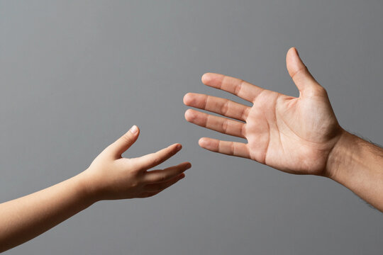 Man and children hands reach toward each other. Child and father hands isolated on gray. Small child's hand reaches for the hand man. Helping hand concept, support. Helping hand outstretched.