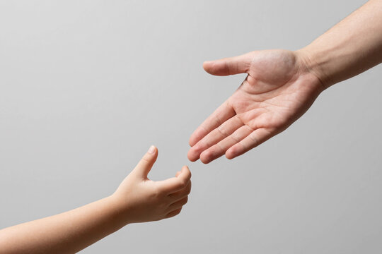 Man and children hands reach toward each other. Child and father hands isolated on gray. Small child's hand reaches for the hand man. Helping hand concept, support. Helping hand outstretched.