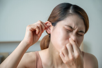 Naklejka premium Asian woman having ears plugged problem. Try to blow out of her nose gently while pinching her nostrils closed and keeping her mouth shut.