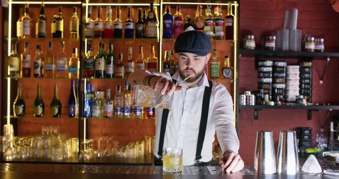 Alcohol drink. Cocktail glass. Skillful bearded male bartender straining liquid using sieve ice cubes at bar counter.