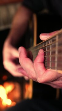 Slow zoom in of a man playing acoustic guitar by the fireplace. A guitar fretboard. Man strumming a guitar. Close-up: plucking a guitar by the hearth. Artist playing music. Musician tuning the guitar.