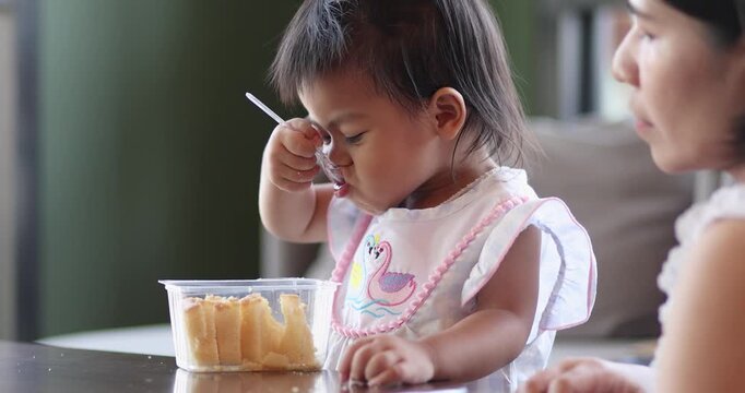 Child feeding snack independently, A little child feeds itself, while mother claps her hands, expressing family love, learning, care, and warm bonding moments, Thai Asian