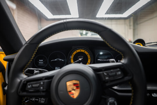 Driver's eye view inside a Porsche 911 Carrera GTS shows crest wheel, yellow tachometer marked GTS, five gauges, digital readouts, and Sport Chrono clock in a garage.