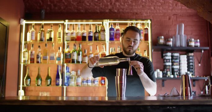 Cocktail mixing. Expert barman. Skillful bearded male bartender pouring alcohol beverage syrup using professional shaker at workplace.