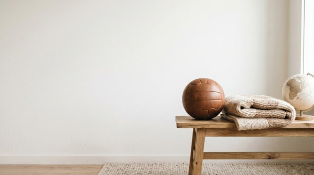 Vintage leather soccer ball with knitted blanket and globe on wooden bench in minimalist interior for travel and sports decor concept