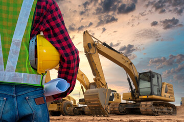 Construction Site Vision: A construction worker, clad in a safety vest and holding blueprints, stands with heavy machinery on a dusty site under a dramatic sky, signifying progress and development. © Rassarin