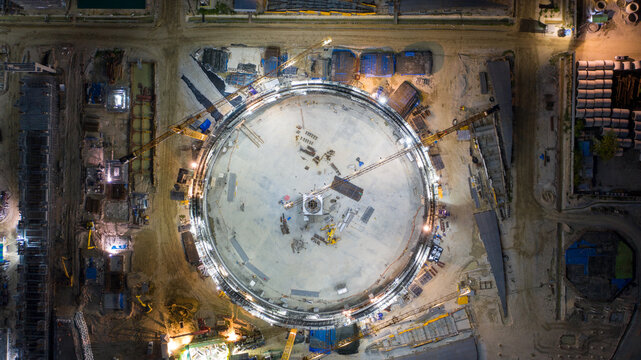 Industrial Construction Site at Night: An aerial view captures the immense scale of an industrial construction site at night, with a large circular structure at its center.