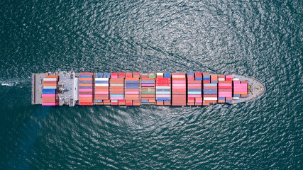Container Ship in Open Sea: An overhead aerial view of a massive container ship carrying numerous colorful cargo containers sailing across the deep blue, wavy ocean. © Rassarin