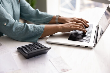 Close up view of woman typing on laptop at desk with documents and calculator, focused on...