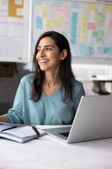 Obraz premium Happy professional woman sits at desk with open laptop holding documents, review data, feel satisfied with project progress, sales growth, take break, thinks on perspectives, career and opportunities