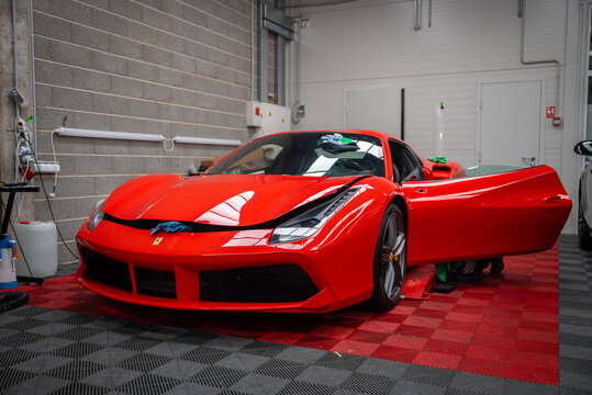 Ferrari 488 Spider sits on a red and black checkered floor with door open. Detailing cloths rest on windshield and hood. Prancing horse badge and LED lights show.