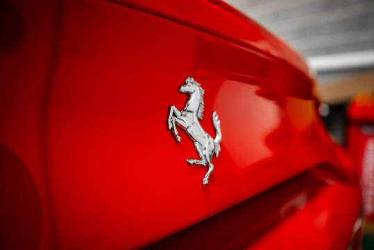 Tight shallow focus shows the chrome prancing horse on a Ferrari 488 Spider near a modern building, soft natural light reflects on sculpted panel lines and glossy paint.