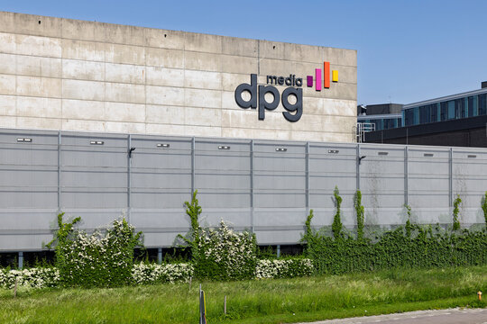 Amsterdam, Netherlands - 23 May 2026 - Exterior view of the DPG Media headquarters building featuring the company logo on a concrete wall behind a fence with green plants.