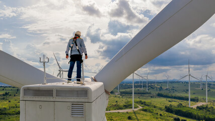 Wind Turbine Maintenance: A lone technician wearing a safety harness stands atop a wind turbine. © Rassarin