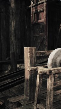 A millstone rests on a wooden frame inside an old structure. Heavy wooden posts support it, and the space is dimly lit. Surrounding walls show signs of age and wear.