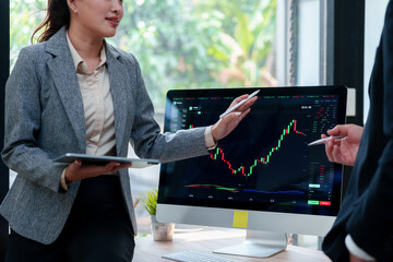 Business executive pointing at a computer screen displaying a stock market chart, discussing investment strategies with a colleague © Crystal