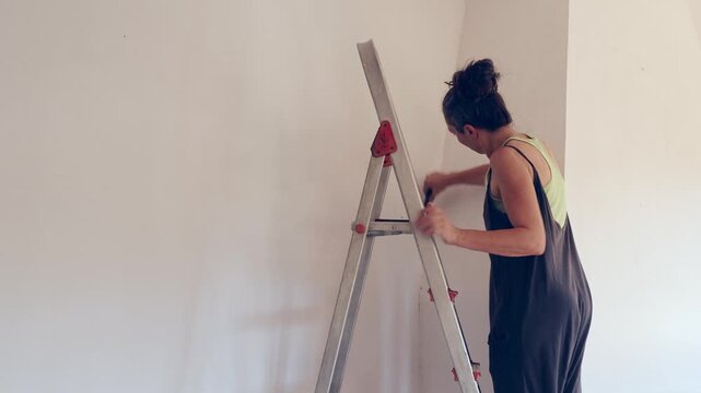 DIY home renovation woman smoothing interior wall on ladder