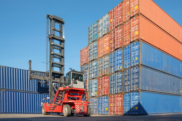 Container Stacking: A robust forklift mechanism stacks colorful shipping containers in a logistics hub, symbolizing global trade and efficient cargo movement under a clear blue sky. © Rassarin